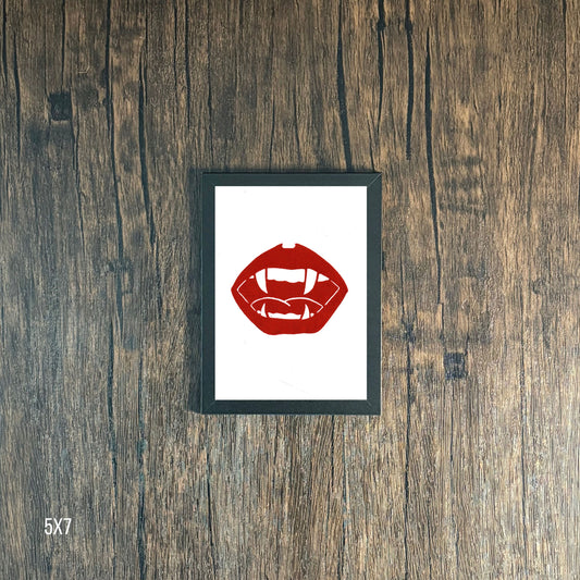 Framed Red lips and vampire fangs graphic on white paper against a wooden background