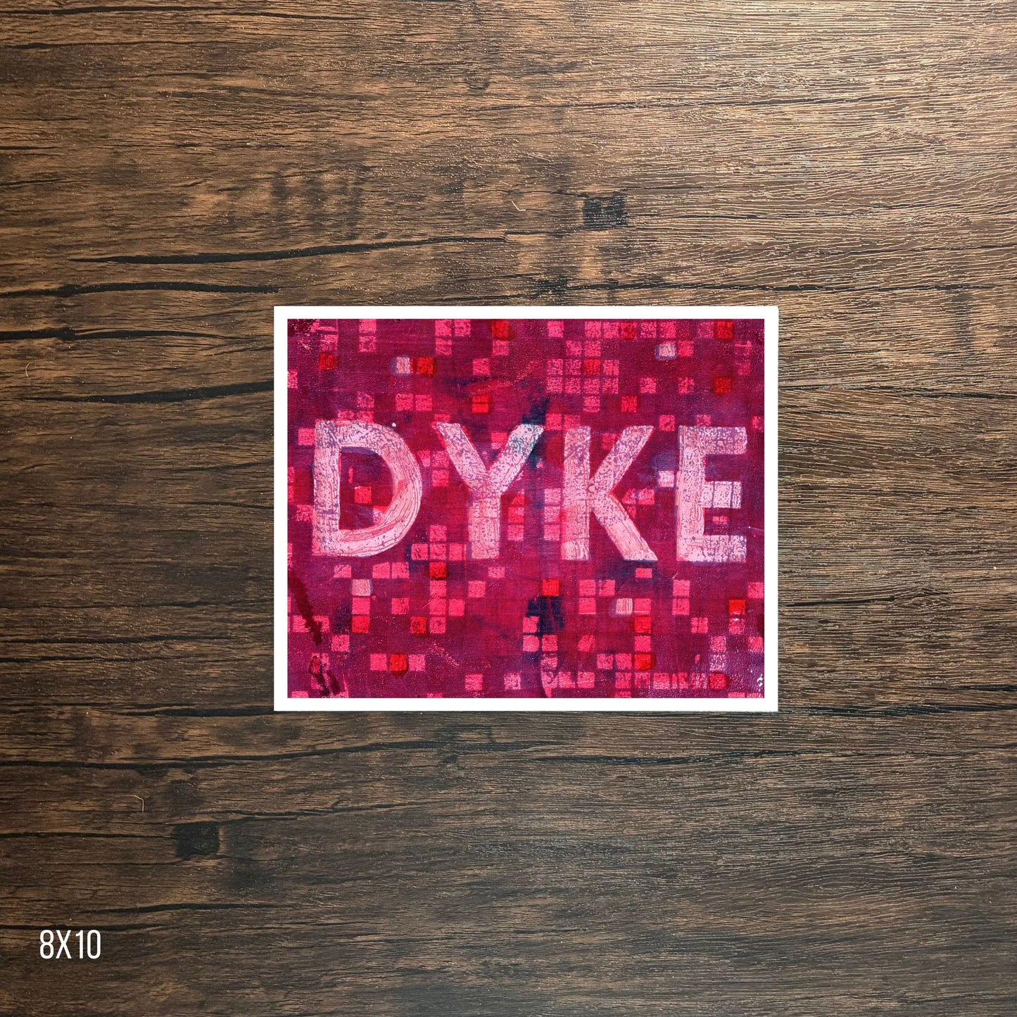 Poster with 'DYKE' text on a pink mosaic pattern against a wooden background