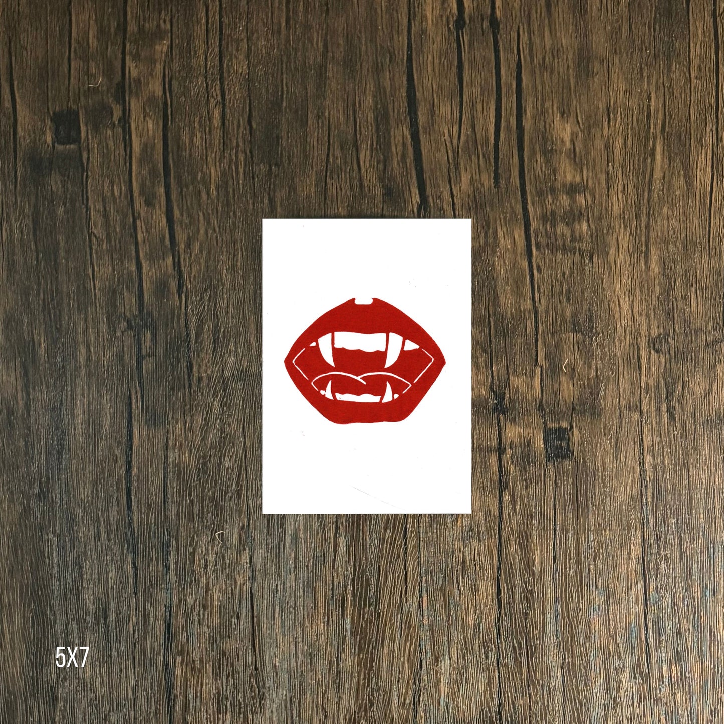 Red lips and vampire fangs graphic on white  paper against a wooden background