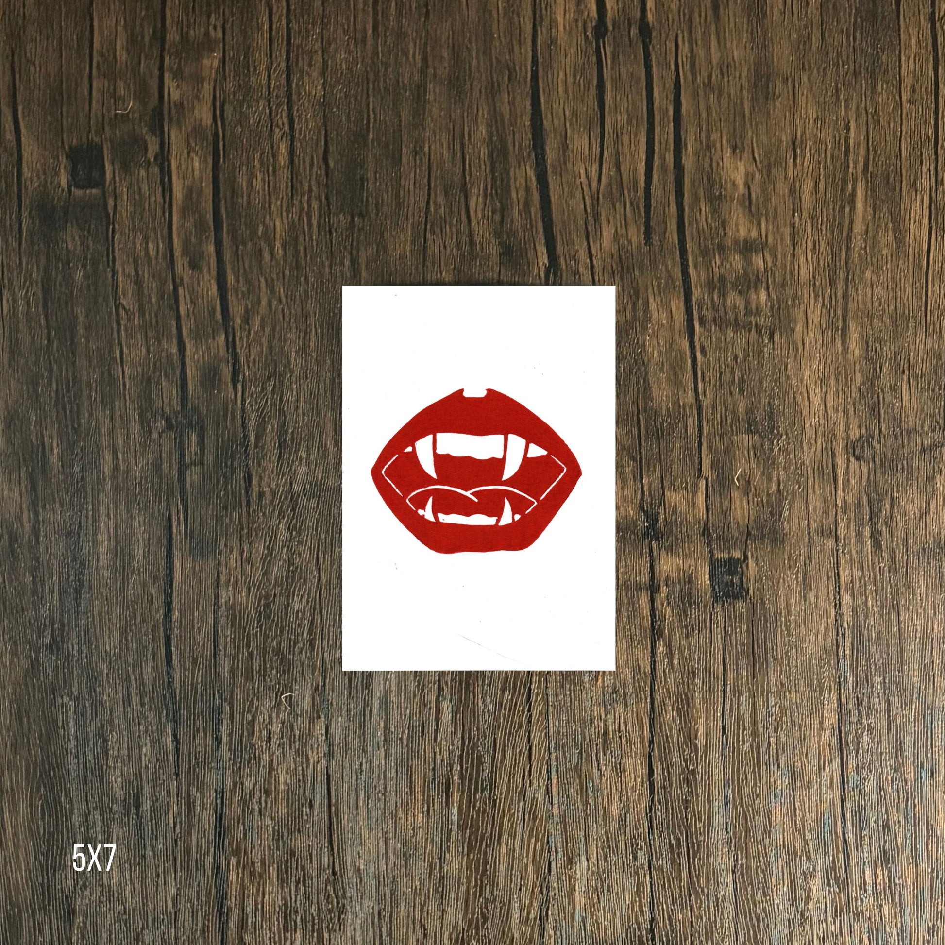 Red lips and vampire fangs graphic on white  paper against a wooden background