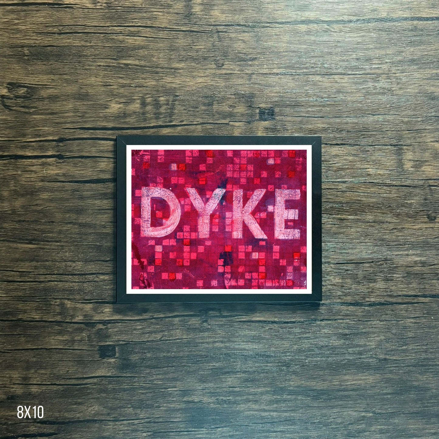 Framed poster with 'DYKE' text on a pink mosaic pattern against a wooden background