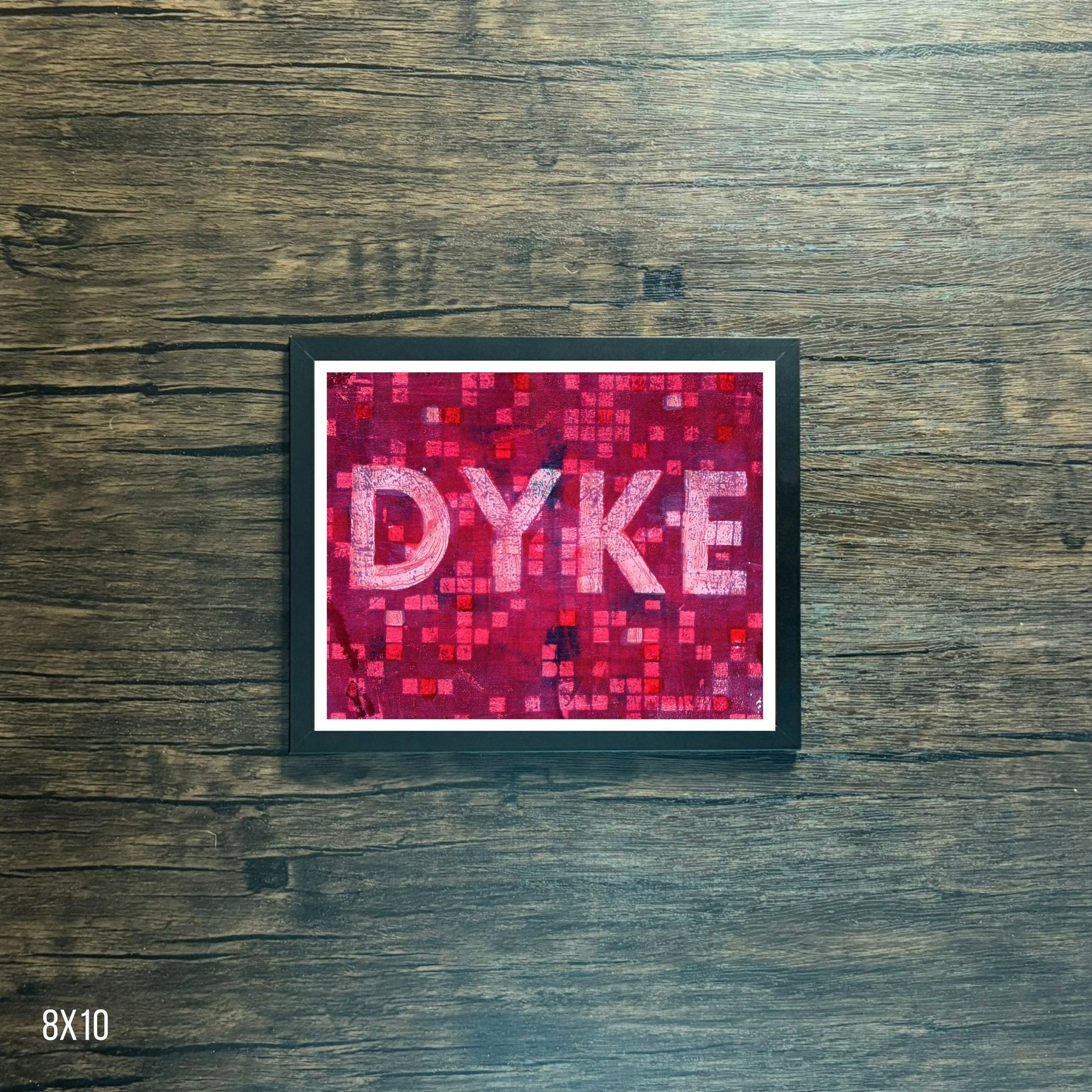 Framed poster with 'DYKE' text on a pink mosaic pattern against a wooden background