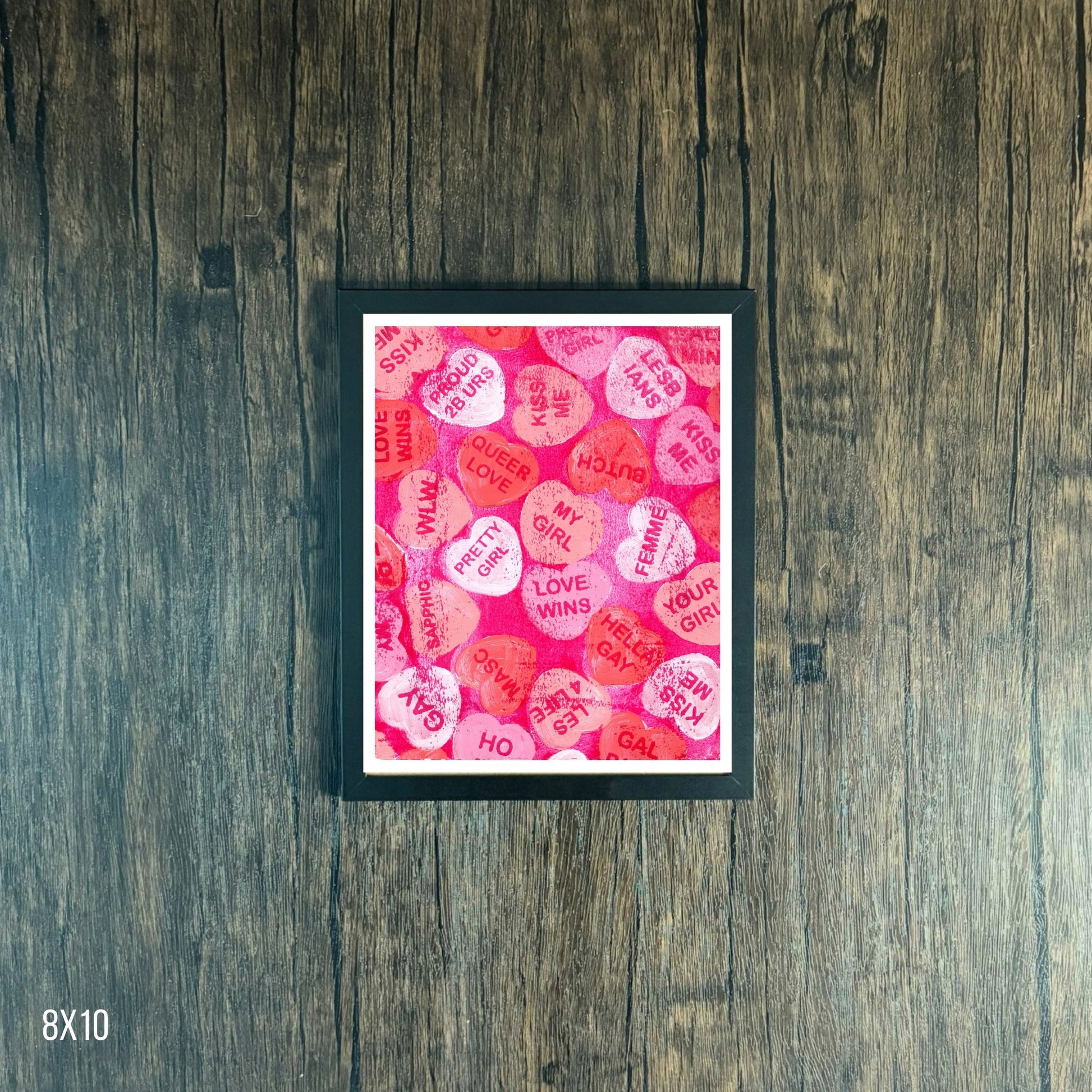 Framed artwork with pink and red text heart pattern on a wooden surface