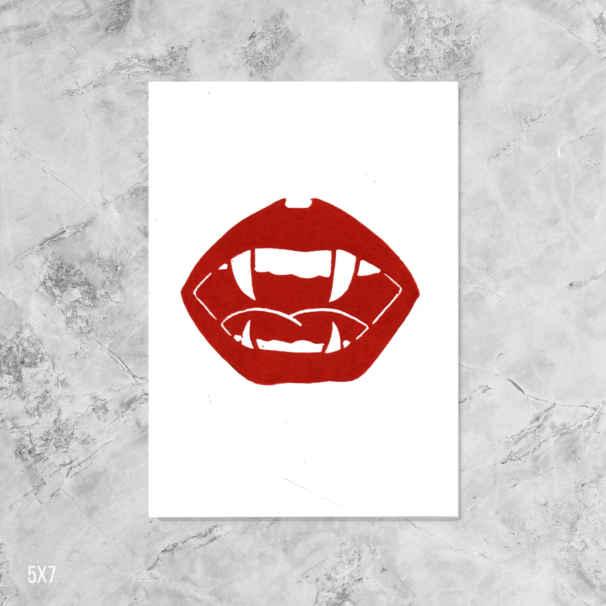 Red lips and vampire fangs graphic on white  paper against a marble background