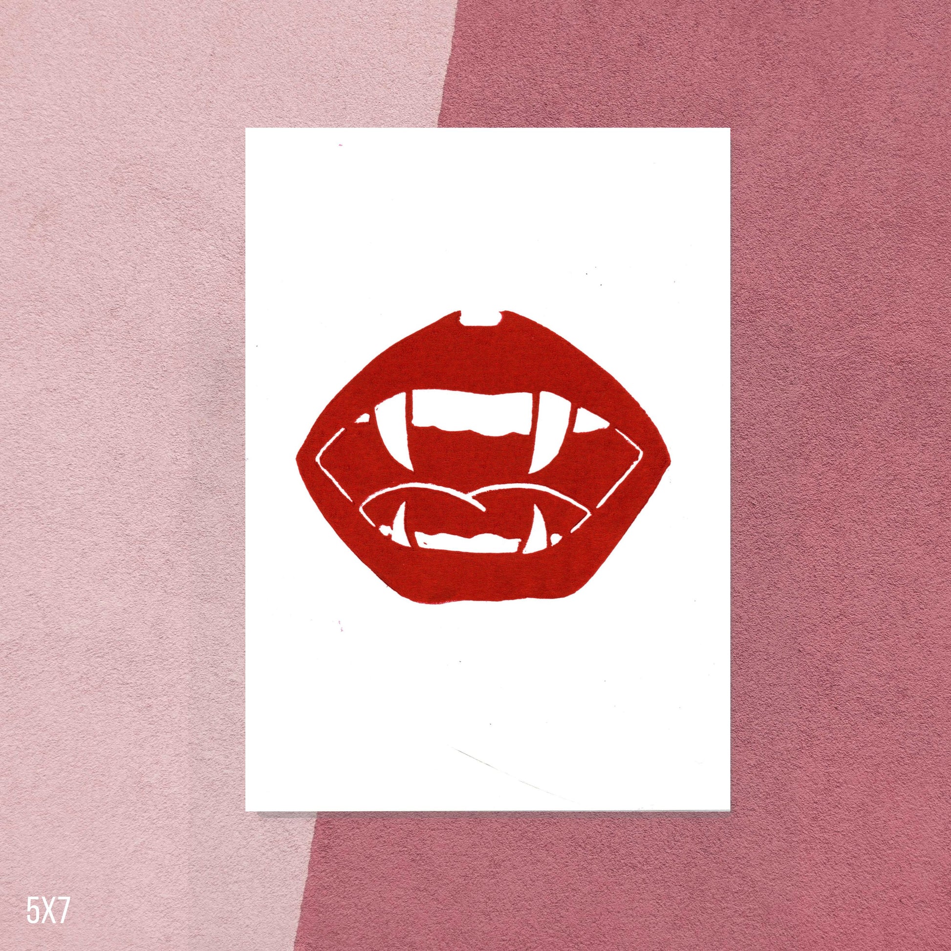 Red lips and vampire fangs graphic on white  paper against a pink background