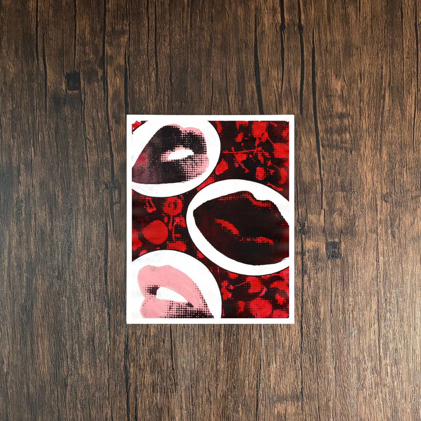 Poster with red and black abstract design of lips and cherries on a wooden surface