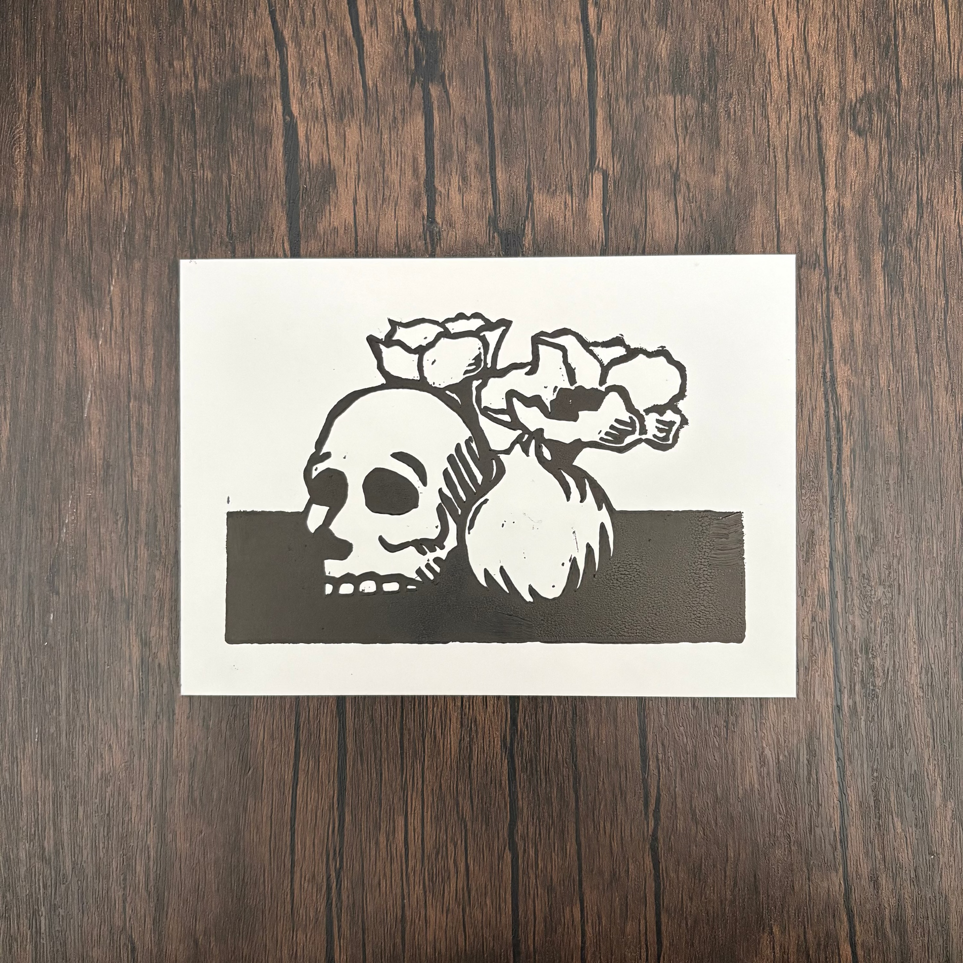 Linocut print of a skull, flowers, and pomegranate on a dark background.